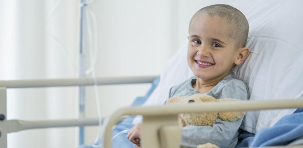 A little boy with a shaved head is smiling as he is laying on a hospital bed.